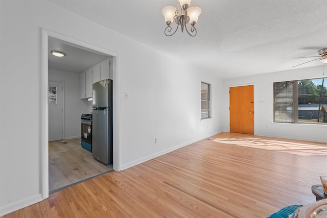 unfurnished living room with a textured ceiling, light wood-style flooring, baseboards, and ceiling fan with notable chandelier