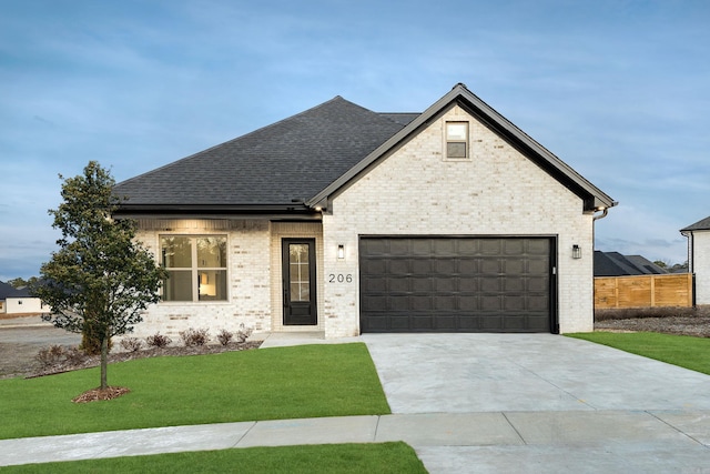 view of front facade featuring driveway, roof with shingles, an attached garage, a front lawn, and brick siding