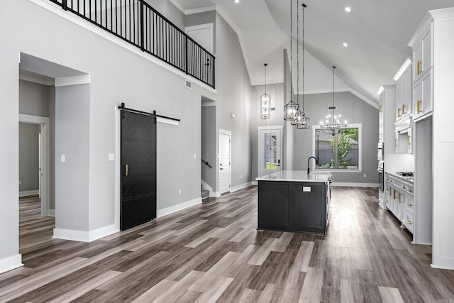 kitchen with dark wood-style floors, a center island with sink, light countertops, a barn door, and white cabinetry