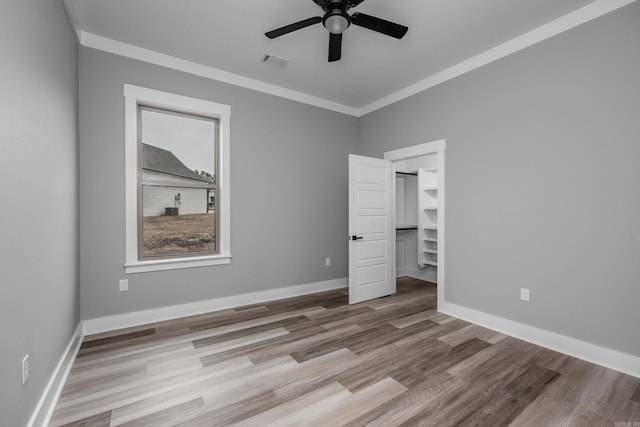 unfurnished room with wood finished floors, a ceiling fan, visible vents, baseboards, and ornamental molding