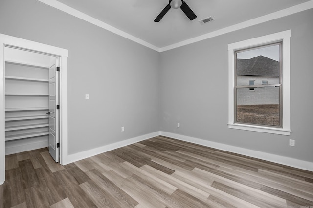 unfurnished bedroom with wood finished floors, visible vents, baseboards, ornamental molding, and a walk in closet