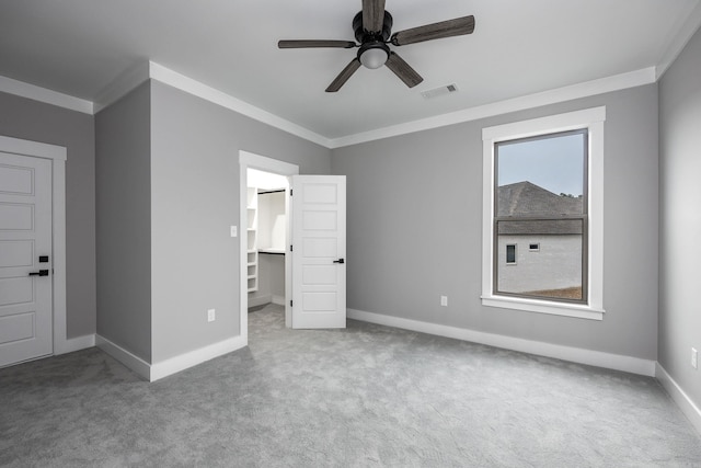 unfurnished bedroom featuring visible vents, baseboards, a spacious closet, ornamental molding, and carpet