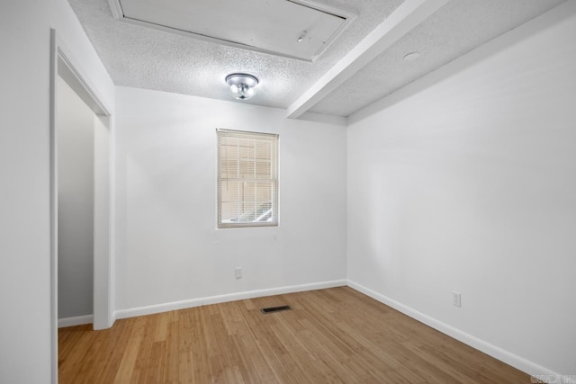 empty room featuring baseboards, a textured ceiling, visible vents, and wood finished floors