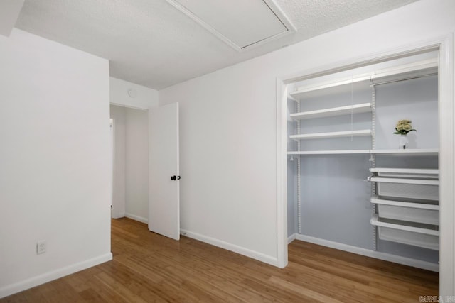 unfurnished bedroom featuring a closet, a textured ceiling, baseboards, and wood finished floors