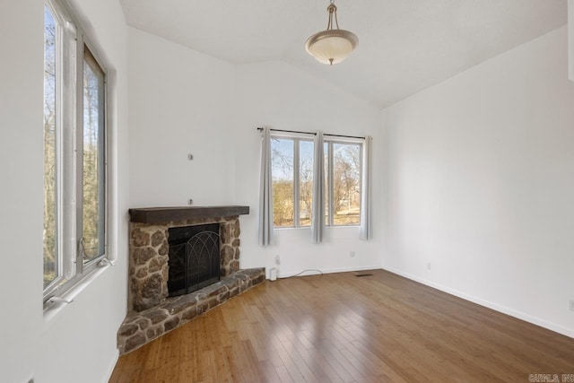 unfurnished living room featuring lofted ceiling, baseboards, a stone fireplace, and hardwood / wood-style floors