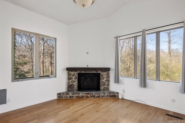 unfurnished living room featuring baseboards, visible vents, wood finished floors, vaulted ceiling, and a stone fireplace