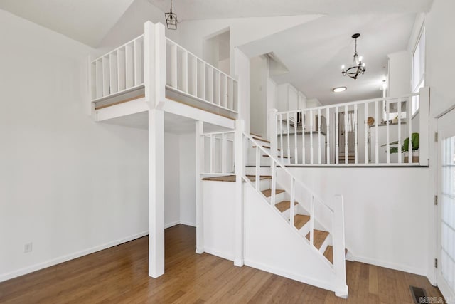 stairs with a chandelier, lofted ceiling, baseboards, and wood finished floors