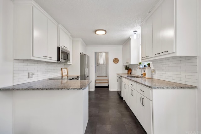 kitchen with light stone counters, appliances with stainless steel finishes, white cabinets, a sink, and a peninsula