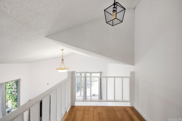 corridor with light wood-style floors, lofted ceiling, and a textured ceiling