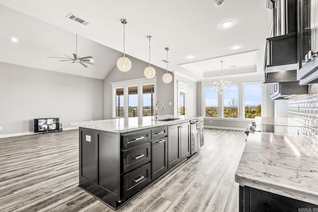 kitchen with light wood-style flooring, a sink, visible vents, dark cabinetry, and a center island with sink