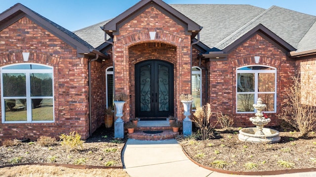 doorway to property featuring brick siding, roof with shingles, and french doors