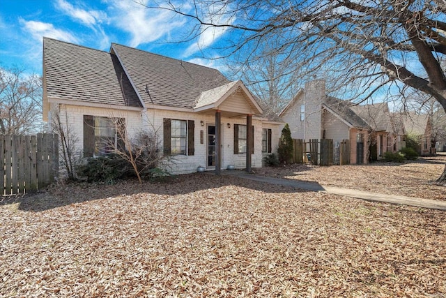 view of front of house with a shingled roof, fence, and brick siding