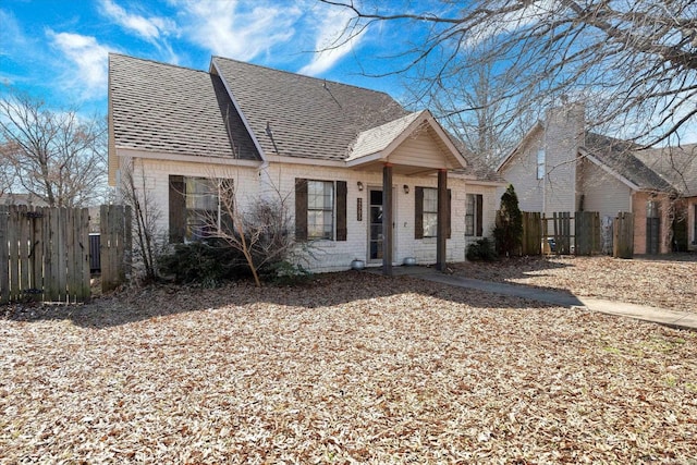 view of front of house with a shingled roof, fence, and brick siding