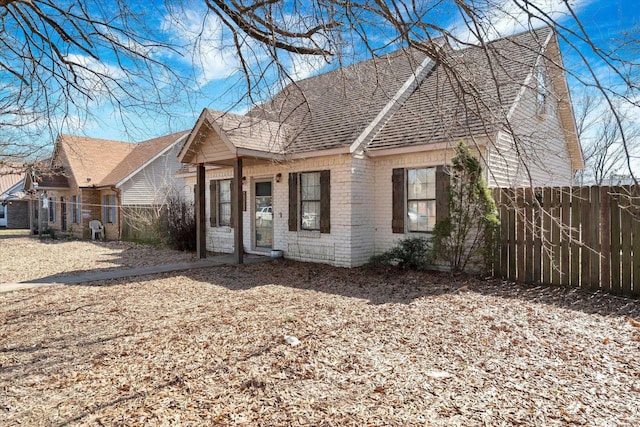 view of front of property featuring brick siding, roof with shingles, and fence