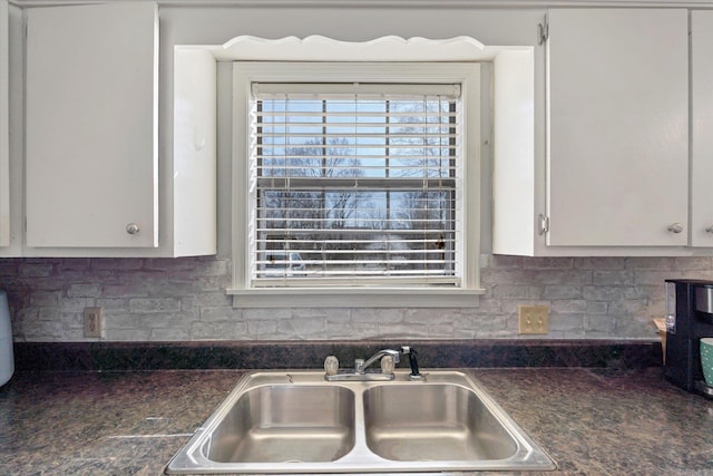 kitchen featuring tasteful backsplash, dark countertops, a sink, and white cabinets