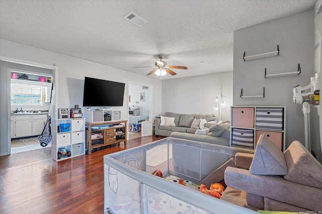 living room with ceiling fan, a textured ceiling, wood finished floors, and visible vents