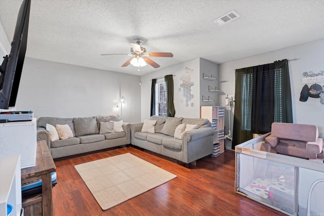 living room with a textured ceiling, wood finished floors, visible vents, and a ceiling fan