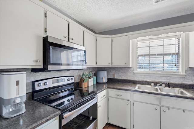 kitchen with appliances with stainless steel finishes, dark countertops, a sink, and tasteful backsplash