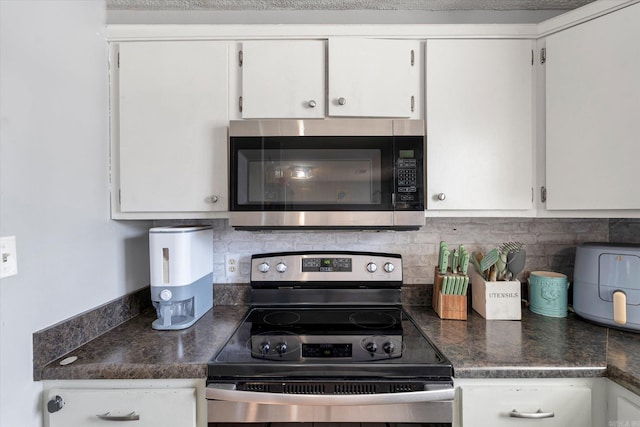 kitchen with dark countertops, white cabinetry, appliances with stainless steel finishes, and backsplash