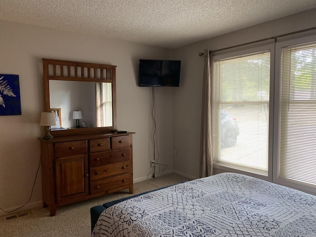 bedroom with a textured ceiling, baseboards, visible vents, and light colored carpet