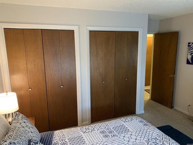 bedroom with light carpet, a textured ceiling, baseboards, and two closets