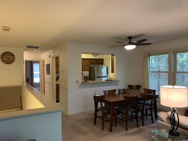 dining room with light carpet, a textured ceiling, plenty of natural light, and visible vents