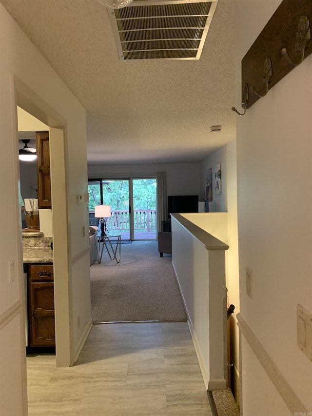 hall with a textured ceiling, an upstairs landing, visible vents, and baseboards