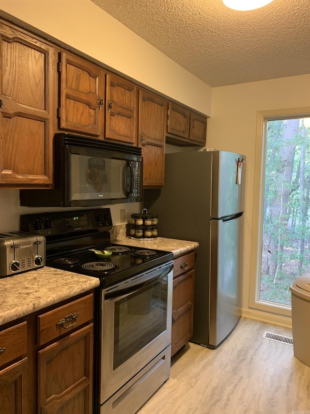 kitchen featuring a textured ceiling, a toaster, light countertops, appliances with stainless steel finishes, and light wood finished floors