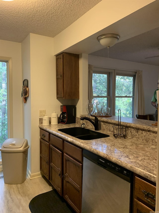 kitchen featuring light wood finished floors, light countertops, a sink, a textured ceiling, and dishwasher