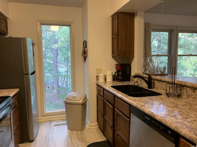 kitchen featuring light wood finished floors, stainless steel dishwasher, a sink, and visible vents