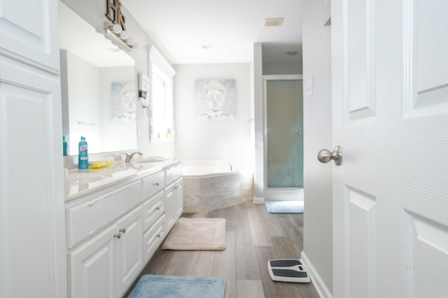 bathroom featuring double vanity, a stall shower, wood finished floors, and a bath