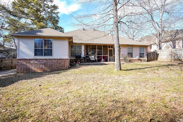 rear view of house featuring a yard, brick siding, fence, and a sunroom