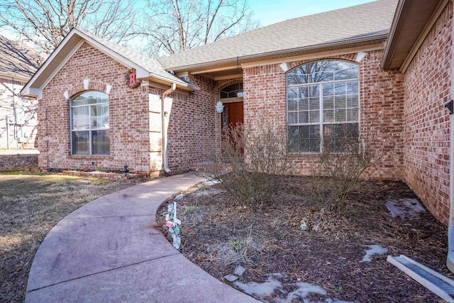 property entrance featuring roof with shingles and brick siding