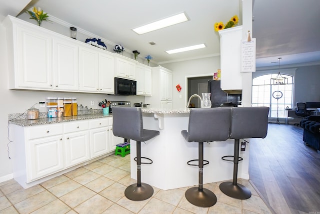 kitchen with black microwave, a breakfast bar, crown molding, fridge, and white cabinetry