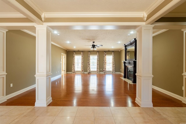 unfurnished living room featuring light tile patterned floors, a glass covered fireplace, ceiling fan, crown molding, and ornate columns