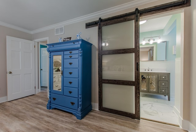 interior space with visible vents, a barn door, ornamental molding, ensuite bath, and wood finished floors