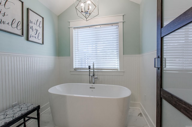 bathroom featuring marble finish floor, a freestanding tub, vaulted ceiling, and a wainscoted wall