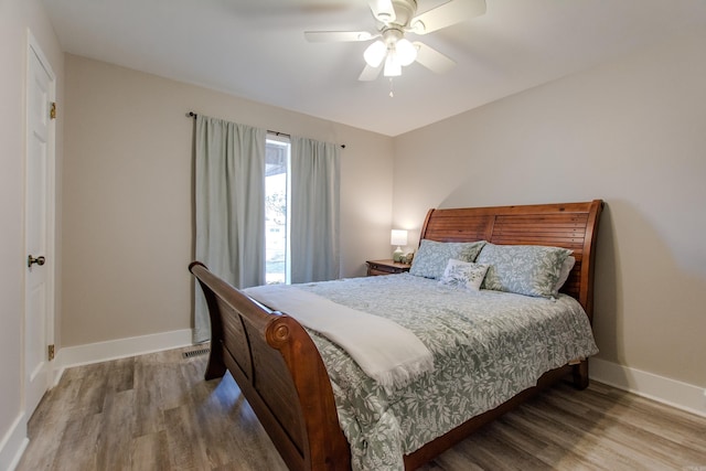 bedroom with a ceiling fan, visible vents, baseboards, and wood finished floors