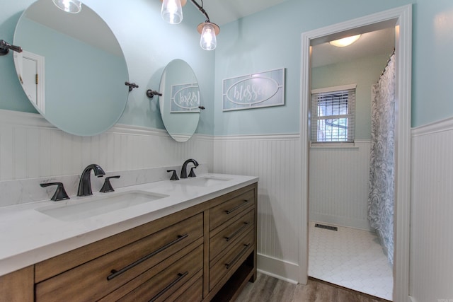 full bathroom featuring a wainscoted wall, a sink, visible vents, and wood finished floors