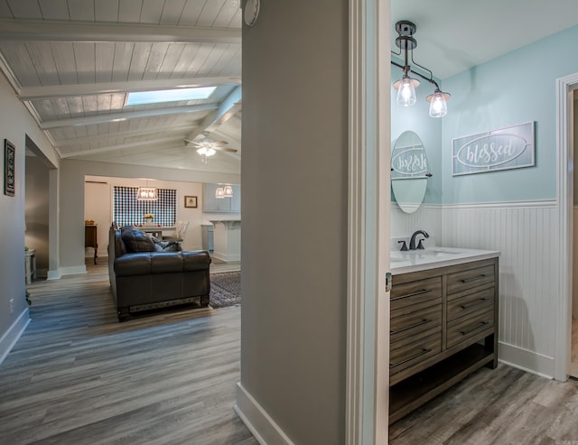 hall featuring vaulted ceiling with skylight, wainscoting, a sink, and wood finished floors