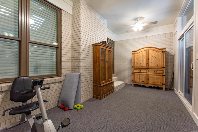 interior space with a ceiling fan, dark carpet, and brick wall