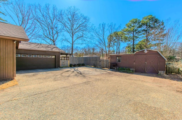 view of yard with a garage, aphalt driveway, a storage unit, fence, and an outdoor structure