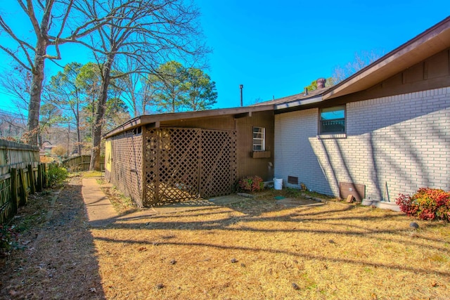 view of side of home with a yard, brick siding, and fence