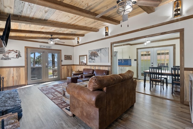 living area with french doors, beam ceiling, wood ceiling, wainscoting, and ceiling fan