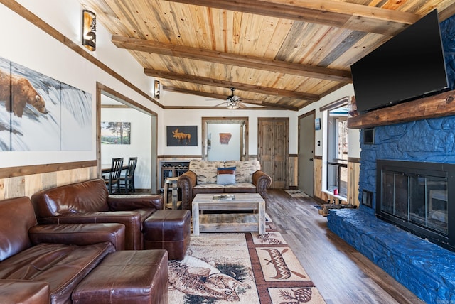 living room featuring vaulted ceiling with beams, a ceiling fan, wood ceiling, a stone fireplace, and wood finished floors