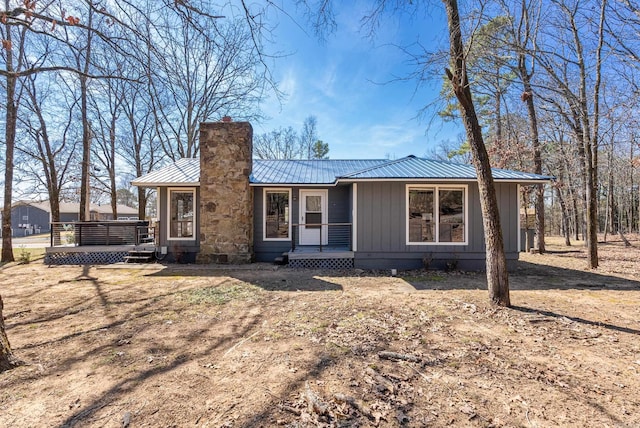 view of front of property with board and batten siding, metal roof, a chimney, and a wooden deck