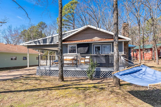 rear view of property with a standing seam roof, metal roof, a chimney, and a lawn