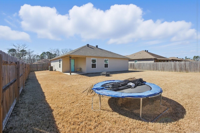 back of house featuring a fenced backyard, a trampoline, and a yard