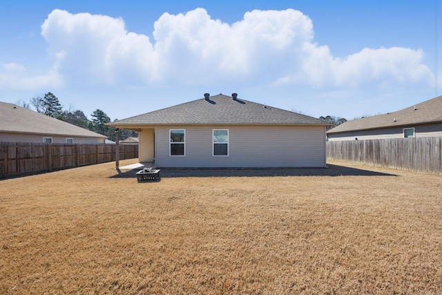 rear view of house with an outdoor fire pit, a shingled roof, a fenced backyard, and a yard