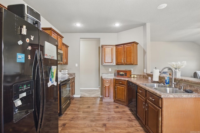 kitchen featuring a peninsula, a sink, light wood-style floors, brown cabinets, and black appliances